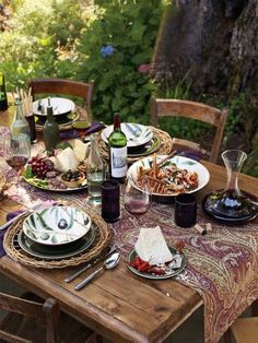 an outdoor table set with plates and wine bottles