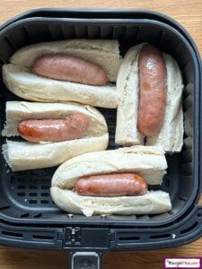 four hotdogs in buns sitting on top of a black plastic container next to a wooden table