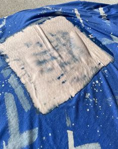 a piece of cloth with blue and white paint splattered on it sitting on the floor