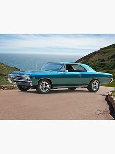 a blue car parked on the side of a road next to the ocean and hills