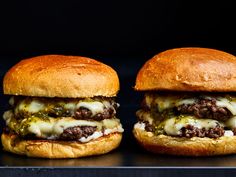 two cheeseburgers with meat and melted cheese on them are sitting side by side