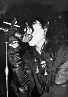 a woman singing into a microphone while holding a pair of gloves on her hand and wearing leather gloves