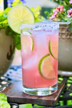 a close up of a drink on a table with flowers and potted plants in the background