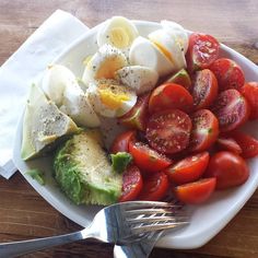 a white plate topped with hard boiled eggs, tomatoes and avocado next to a fork