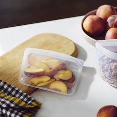 a plastic container filled with sliced peaches on top of a table next to other fruits