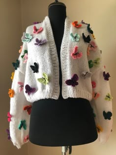 a white sweater with multicolored butterflies on the front and back, sitting on a black mannequin