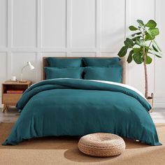 a bed with teal colored linens and pillows in a white room next to a potted plant