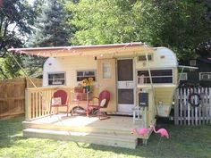 an old camper is parked on the grass with pink flamingos in front of it