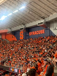 an orange and blue stadium filled with people sitting on the bleachers watching something