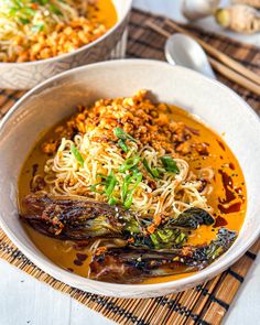 two bowls filled with noodles and vegetables on top of a place mat next to spoons