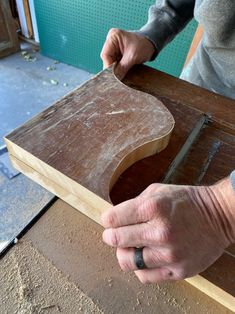 a man is working on a piece of wood in his workshop, with one hand holding the edge