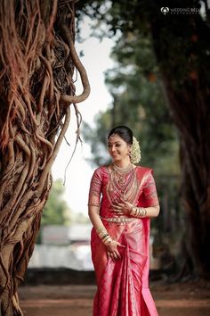 a woman in a red and gold sari standing next to a tree with her hands on her hips