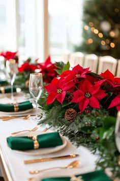 a table set for christmas with poinsettis and greenery