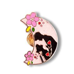 a pink and black cat sitting on top of a crescent shaped broochle with flowers