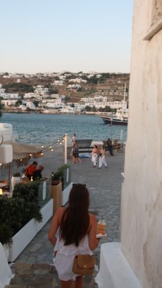 the woman is walking down the stairs towards the water and boats in the harbor behind her