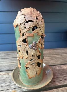 a green vase with leaves on it sitting on a wooden table