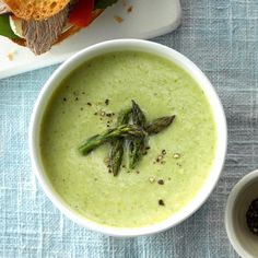 there is a bowl of soup with asparagus in it and bread on the side