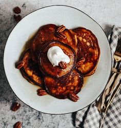 pancakes with pecans and whipped cream are on a white plate next to a fork