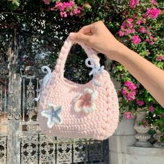 a hand holding a pink crocheted purse in front of a flowered fence