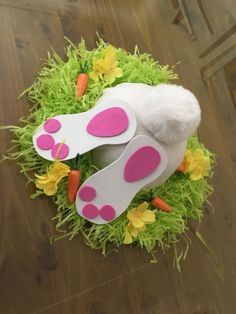 an easter wreath with bunny ears and carrots on the ground next to a wooden floor