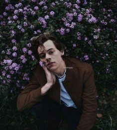 a young man sitting in front of purple flowers with his chin resting on his hand