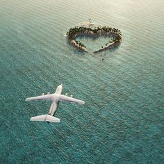 an airplane flying over the ocean with a small island in the shape of a heart