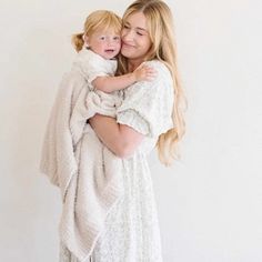 a woman holding a baby wrapped in a blanket while standing next to a white wall