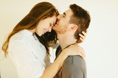 a man and woman are kissing each other in front of a white wall with their arms around each other