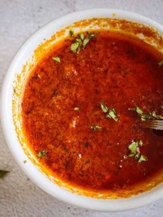 a white bowl filled with tomato sauce and garnished with parsley