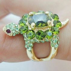 a close up of a person's hand holding a ring with green and yellow stones