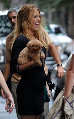 a woman walking down the street with a dog in her lap and people behind her