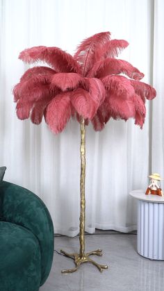 a pink feather palm tree in a living room next to a green couch and white curtains