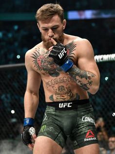 a man with tattoos on his chest standing in front of a cage holding a boxing glove