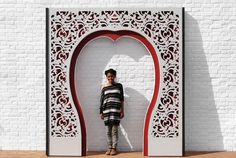 a woman standing in front of a white brick wall with an intricate design on it