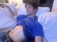 a young man laying on top of a white couch next to pillows and a remote control