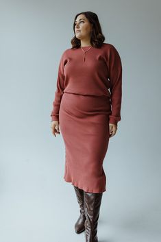 A woman wearing the Mikarose Ribbed Knit Midi Length Pencil Skirt in Smokey Rosewood and a rust-colored sweater, complemented by brown knee-high boots, stands against a plain gray background. Denim Gift, Knit Midi, Earring Sale, Knitting Materials, Bridal Collection, Sales Gifts, Fashion Games, Midi Length, Drawstring Waist