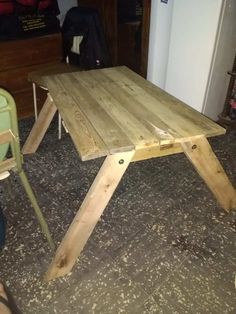 a wooden table sitting on top of a kitchen floor next to a green plastic chair