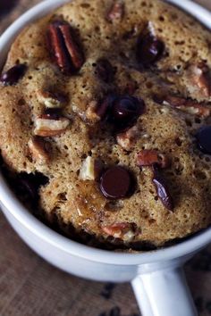 a cookie with chocolate chips and pecans in a white cup on a wooden table