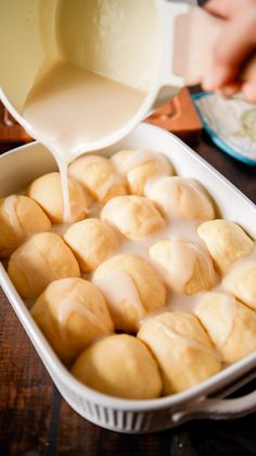 a pan filled with rolls covered in icing being drizzled on top of it