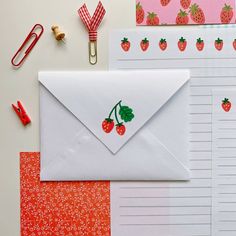 an envelope with strawberry stickers on it next to other stationery items and paper clips