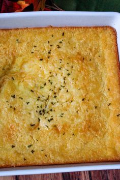 a square casserole dish with cheese and herbs in it on a wooden table