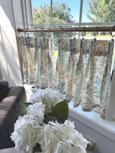 a vase with white flowers sitting on a window sill in front of a curtain