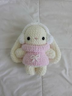 a crocheted stuffed animal wearing a pink dress on top of a white sheet