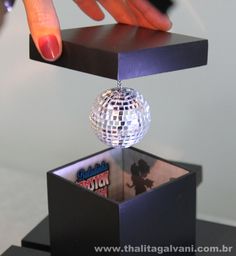 a person is touching the disco ball on top of a black box with its reflection in it