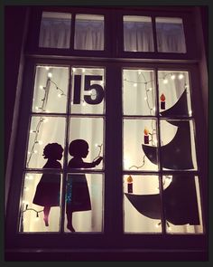 the silhouettes of two children are seen through a window with christmas lights on it