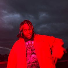 a man with dreadlocks standing in front of a dark cloudy sky and holding a cell phone