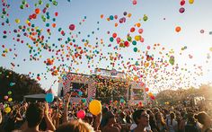 a large group of people at a festival with balloons in the air and onlookers watching