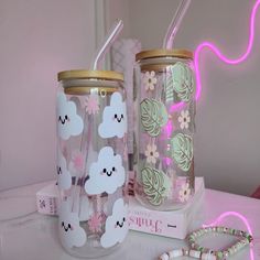 two glass cups with straws in them sitting on a table next to a neon light