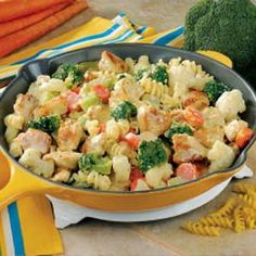 a skillet filled with chicken, broccoli and cauliflower on top of a table