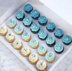 a box filled with blue and white cupcakes on top of a marble counter